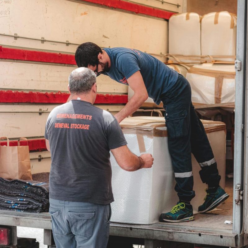 Faceless removal porters in uniform unloading big white boxes off lorry while working in delivery service